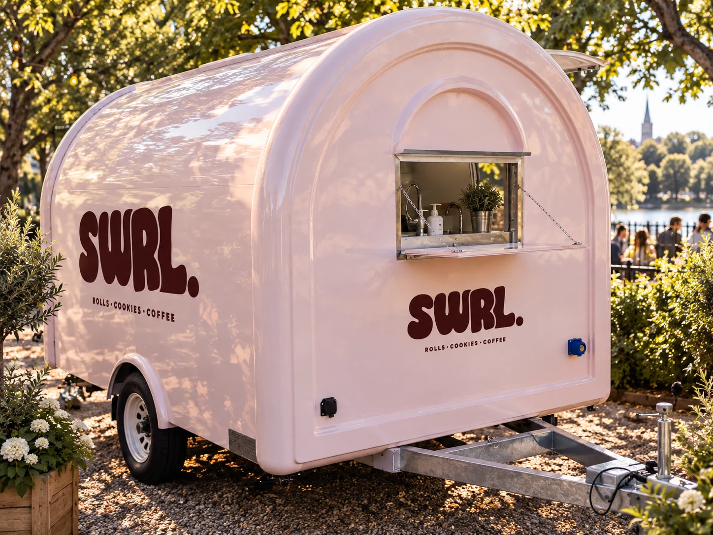 The rounded pink side of the SWRL truck with its small hatch open beneath leafy trees